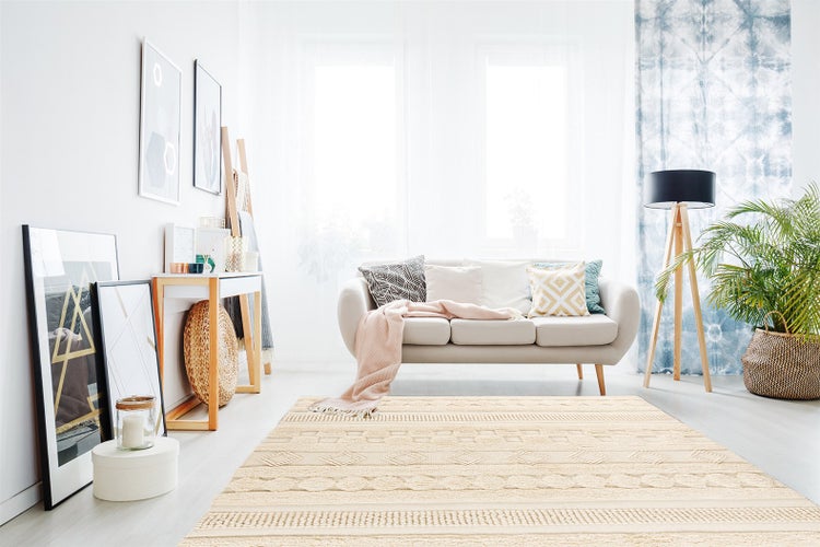 Beigefarbener Teppich mit geometrischen Mustern in einem hellen, modernen Wohnzimmer mit Sofa, Stativ-Stehleuchte und Zimmerpflanzen.