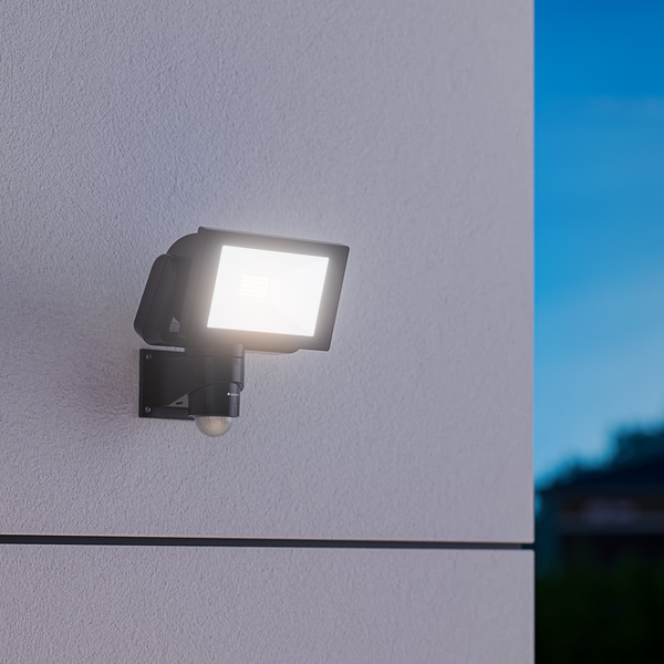 LED Strahler mit Bewegungsmelder von Steinel an einer Hauswand montiert bei Dämmerung.
