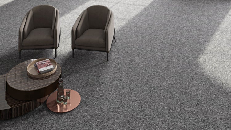 Moderner Wohnbereich mit großflächigem grauem Teppichboden, zwei Polstersesseln und einem abgestuften Couchtisch in hellem Ambiente.