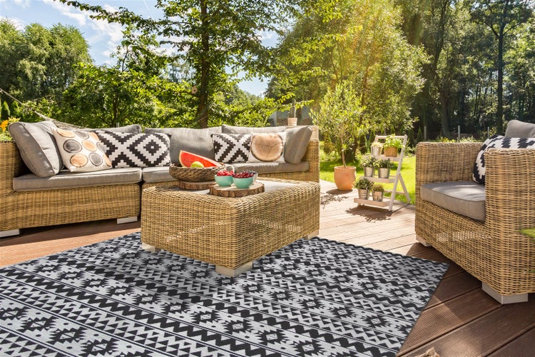 Outdoorteppich mit geometrischem Muster auf einer sonnigen Holzterrasse mit Polyrattan-Lounge-Möbeln und Blick ins Grüne.