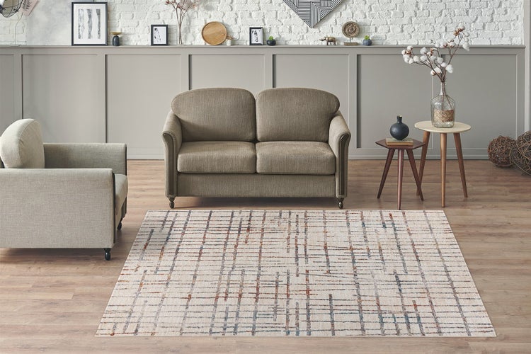 Modernes, helles Wohnzimmer mit Teppich im Gittermuster, taupefarbenem Sofa, grauem Sessel und Beistelltischen vor einer weißen Backsteinwand.