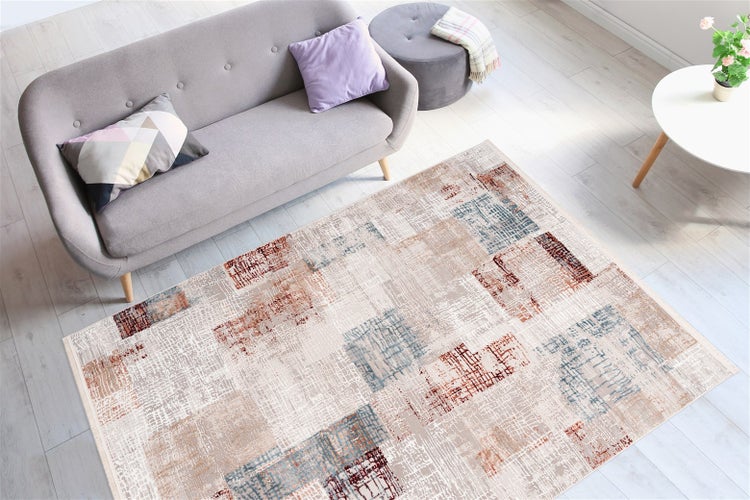 Modernes, helles Wohnzimmer mit abstrakt gemustertem Teppich auf hellem Boden, einem grauen Sofa mit Zierkissen und einem grauen Hocker.