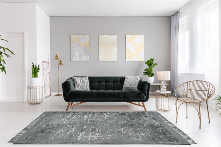 Moderner Wohnraum mit dunkelgrünem Samtsofa, grauem Teppich im Vintage-Look, goldenen Beistelltischen und abstrakter Wandkunst.