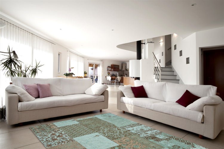Helles Wohnzimmer mit zwei Sofas und einem türkisfarbenen Webteppich in Patchwork-Optik auf hellem Fliesenboden.