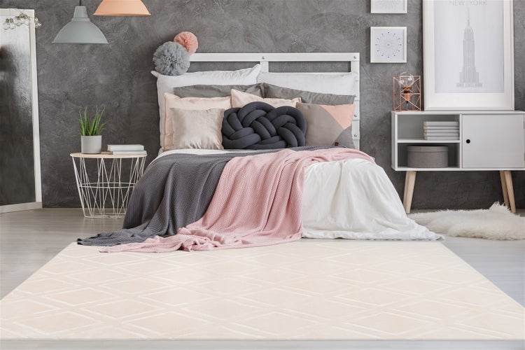 Cremefarbener Teppich mit Rautenmuster in einem modernen Schlafzimmer mit grauem Bett und rosa Accessoires.