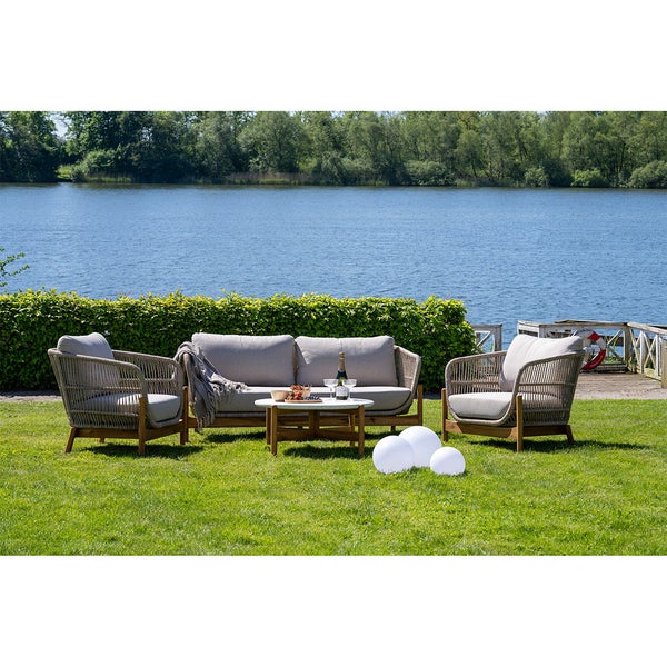 Gartenmöbelset mit Sofa, Sesseln und Tisch auf einer Rasenfläche mit Seeblick