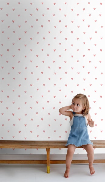 Mädchen sitzt vor einer Wand mit Herz Tapete