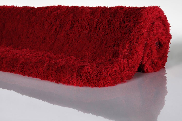 Hochflor-Teppich Shaggy in Rot, flauschige und weiche Oberfläche, teilweise eingerollt.