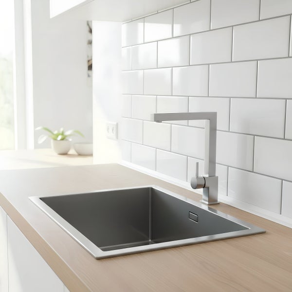 Moderne Küchenspüle aus Edelstahl mit quadratischer Küchenarmatur vor einer weißen Fliesenwand in einer hellen Küche.