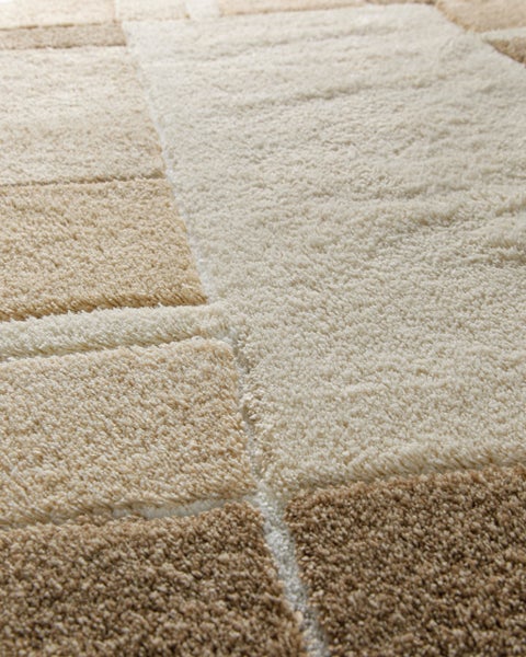 Detailaufnahme eines Hochflor-Teppichs mit beige- und cremefarbenem geometrischem Blockmuster und strukturierter Oberfläche.
