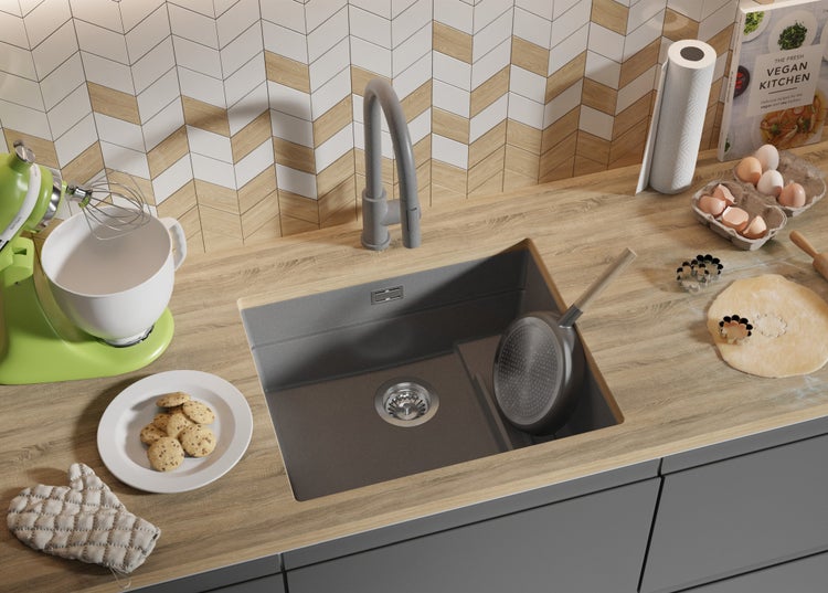 Küchenszene mit Spüle, Armatur, Küchenmaschine, Kochbuch, Zutaten und Backutensilien auf einer Küchentheke.