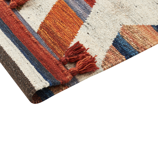 Detailaufnahme eines gewebten Teppichs mit geometrischen Mustern, Streifen und Quasten in Rostrot, Blau und Beige.