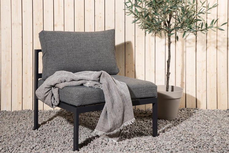 Gartenmöbel Sessel mit Kissen und Decke sowie Olivenbaum im Topf vor Holzwand
