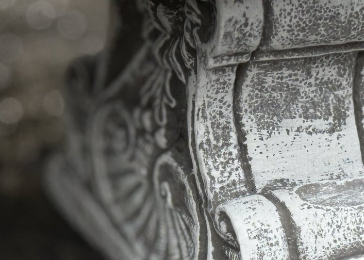 Detailansicht einer verzierten Gartenfigur oder eines Sockels aus Stein mit antiker Optik und detaillierten Ornamenten.
