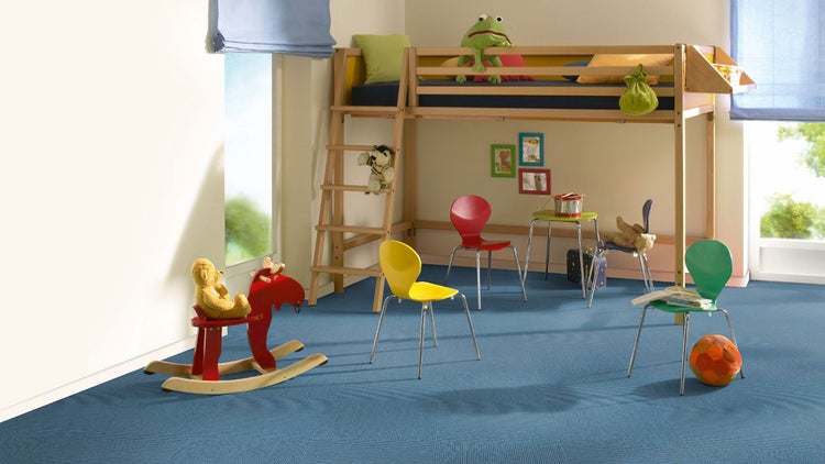 Helles Kinderzimmer mit blauem Teppichboden, einem Hochbett aus Holz und bunten Stühlen.