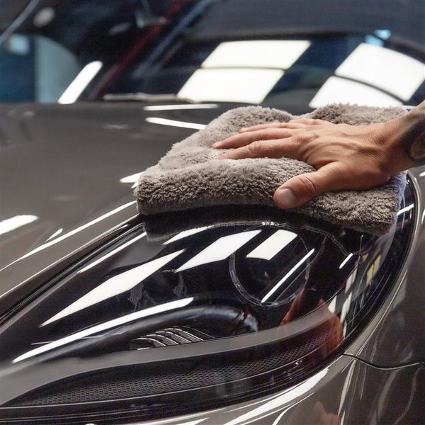 Eine Hand poliert mit einem Mikrofasertuch ein Auto.