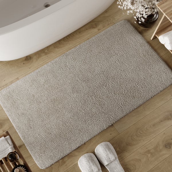 Rechteckige Badematte mit flauschiger Textur auf einem Holzboden neben einer Badewanne in einem hellen Badezimmer.