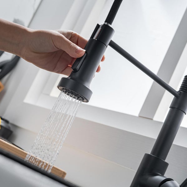 Hand bedient ausziehbare Küchenarmatur mit Wasserstrahl aus dem Brausekopf vor einem Fenster.