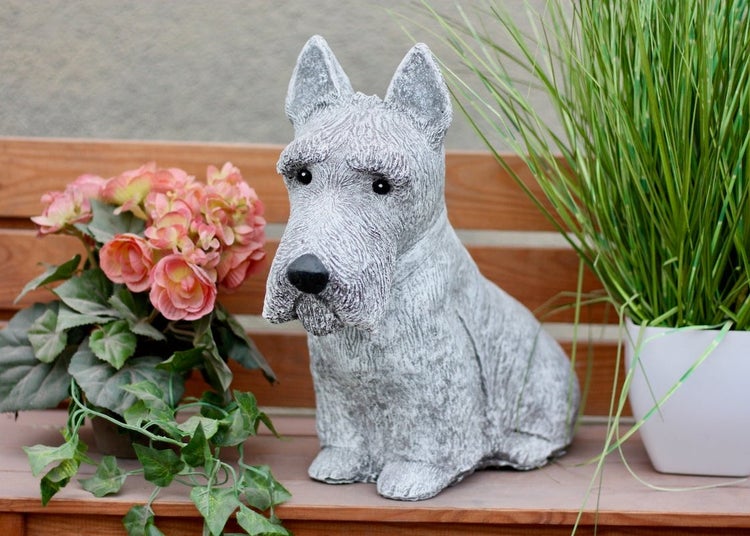 Gartenfigur in Form eines sitzenden Terriers in Steinoptik, dekoriert auf einer Holzbank zwischen Topfpflanzen.