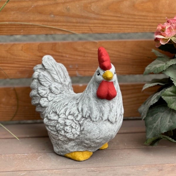 Gartenfigur Huhn in Steinoptik mit rotem Kamm, Kehllappen und gelbem Schnabel auf Holzoberfläche.