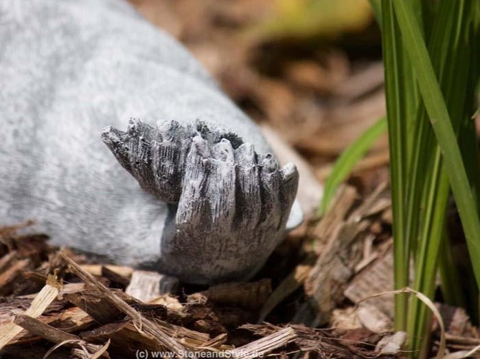 Detailansicht der Pfote einer Steinfigur im Garten auf Rindenmulch