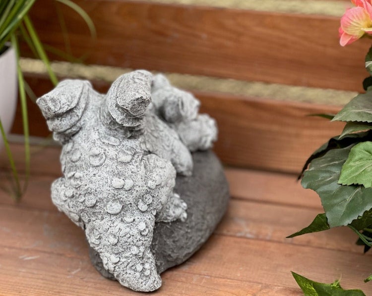 Gartenfigur in Form eines kleinen Drachens aus Steinguss von hinten, sitzend auf einem Stein auf einer Holzterrasse.
