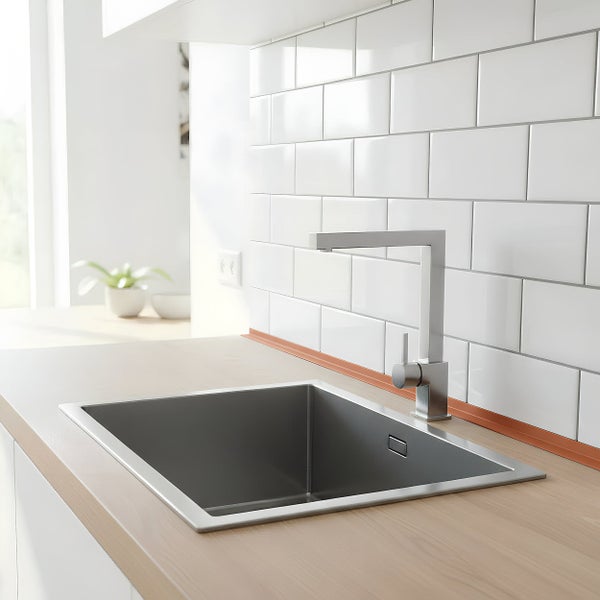 Moderne Küchenspüle aus Edelstahl mit Einhebelmischbatterie in einer hellen Küche mit weißen Wandfliesen im Ziegelverband und Holzoptik Arbeitsplatte