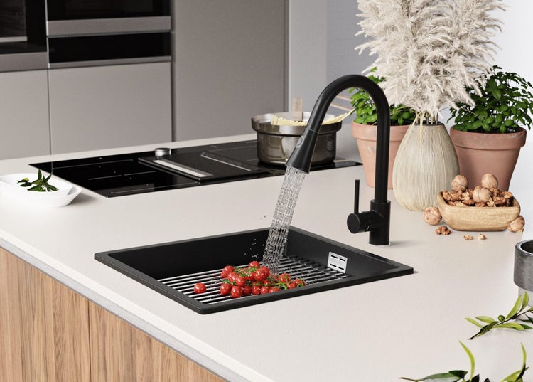 Schwarze Küchenspüle mit Armatur, Abtropfgitter und Tomaten auf einer Küchentheke.