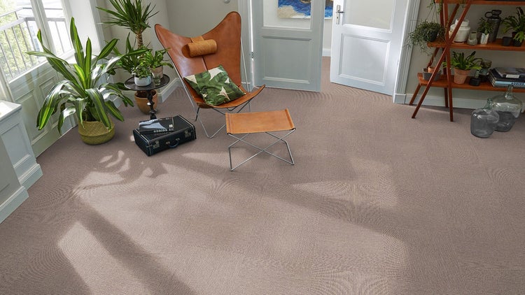 Teppichfliesen in einem hellbraunen Wohnzimmer mit Butterfly-Sessel, Zimmerpflanzen und Holzregal.
