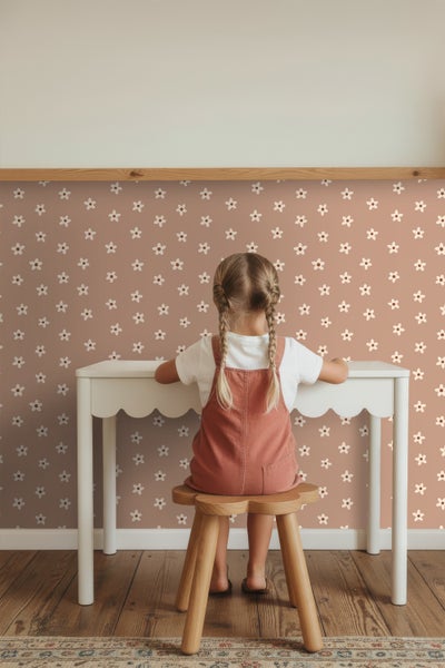 Mädchen sitzt an einem weißen Kindertisch vor einer Wand mit Blumenmuster