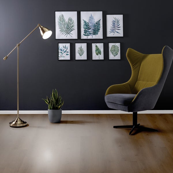 Innenaufnahme eines Wohnzimmers mit Sessel, Stehlampe, Topfpflanze und Wandbildern