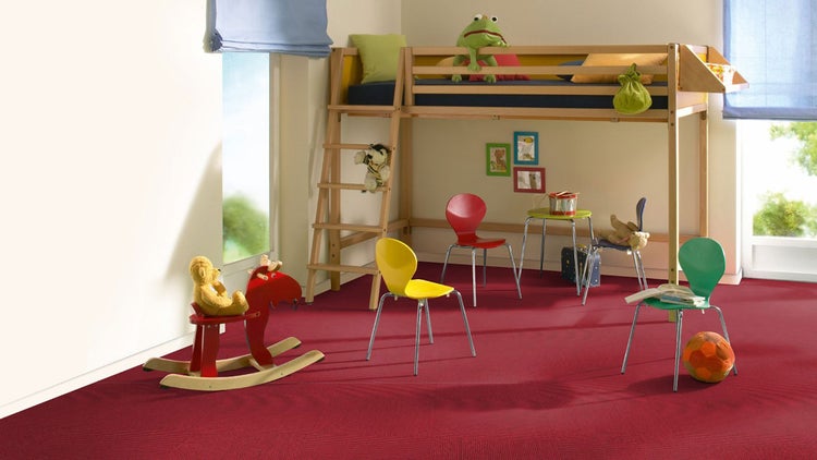Helles Kinderzimmer mit roten Teppichfliesen, einem Hochbett aus Holz, bunten Stühlen und einem Schaukelpferd.