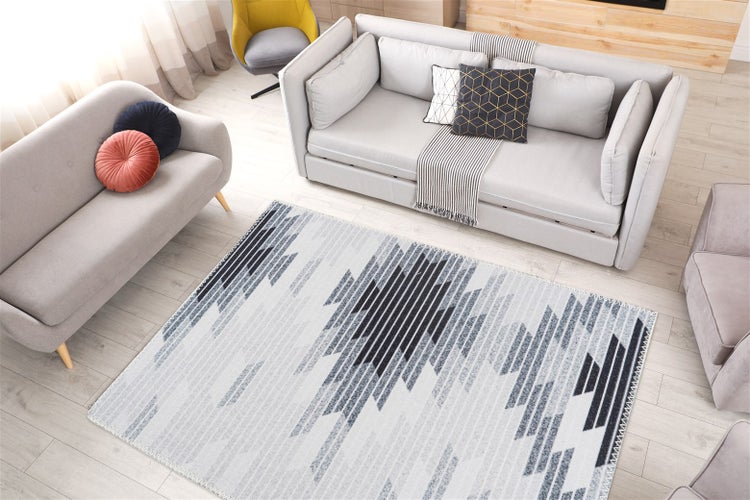 Modernes Wohnzimmer mit geometrisch gemustertem Teppich in Grau und Schwarz auf hellem Holzboden mit grauen Sofas.