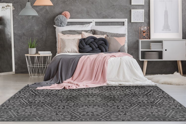 Moderner Teppich mit geometrischem Sechseck-Muster in einem Schlafzimmer vor einem Bett mit Kissen und Decken.