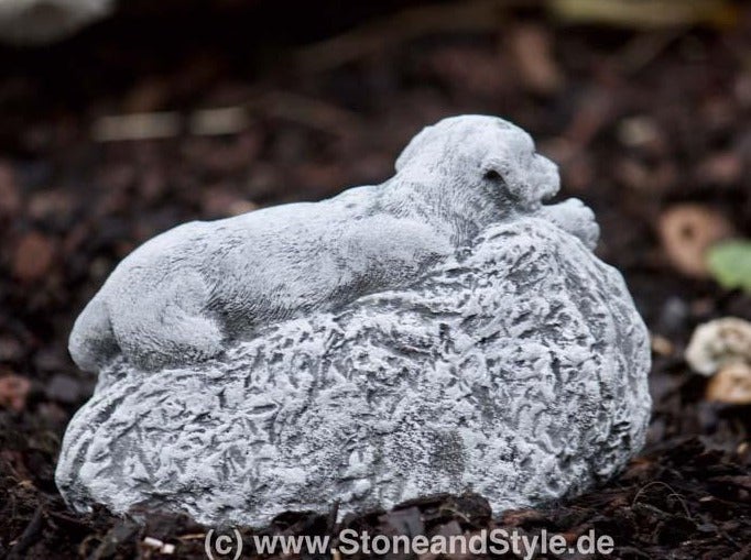 Steinfigur liegender Hund auf einem Felsen als Dekoration für den Garten aus wetterfestem Steinguss