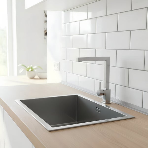 Moderne Küchenspüle aus Edelstahl mit Einhebelmischbatterie in einer Küche mit heller Arbeitsplatte und weißen Fliesenspiegel.
