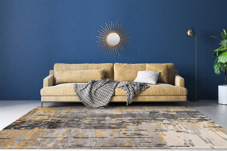 Modern eingerichtetes Wohnzimmer mit beigem Sofa, grau-gelb gemustertem Teppich, Sonnenspiegel an blauer Wand, Stehlampe und Zimmerpflanze.