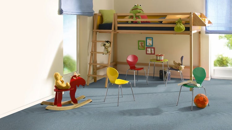 Helles Kinderzimmer mit Teppichfliesen auf dem Boden, einem Hochbett aus Holz, Stühlen und einem Schaukelpferd.