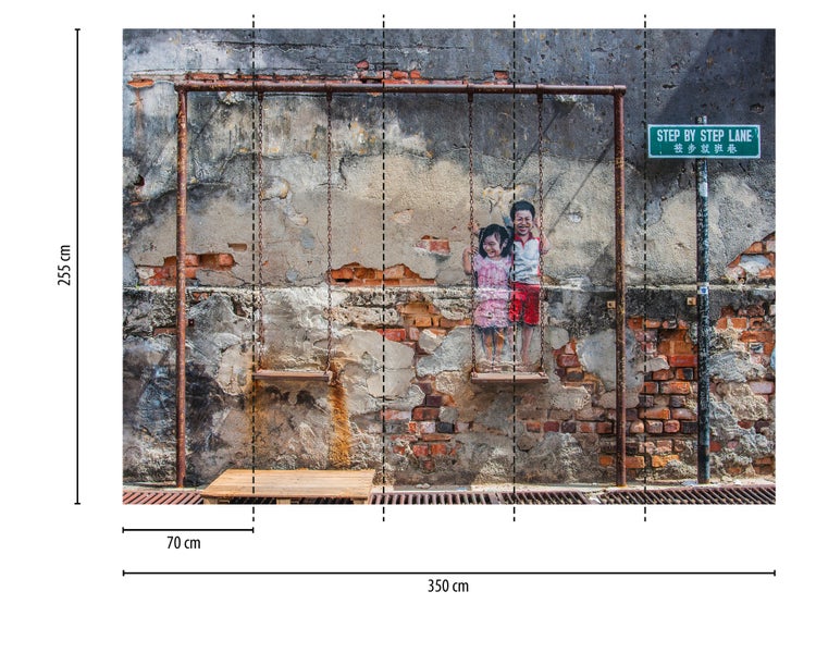 Fototapete mit Street Art Motiv, Kinder auf Schaukel vor einer Ziegelwand, 350 mal 255 Zentimeter.