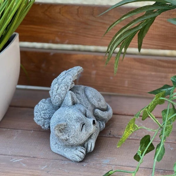 Dekorative Gartenfigur Katze mit Engelsflügeln aus Stein, schlafend dargestellt auf einem Holzuntergrund.