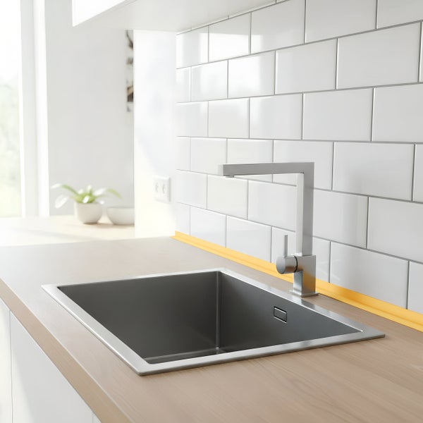 Moderne Küchenspüle aus Edelstahl mit Einhebelmischbatterie in einer hellen Küche mit weißen Wandfliesen und einer Arbeitsplatte in Holzoptik.