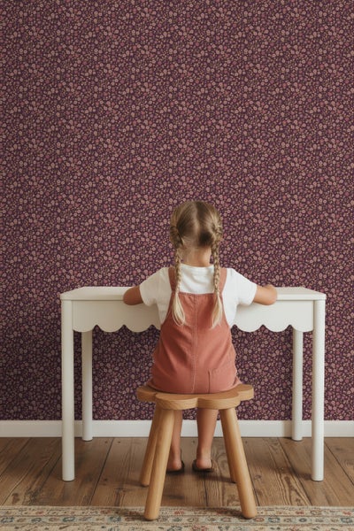 Mädchen sitzt an einem Schreibtisch vor einer floralen Tapete