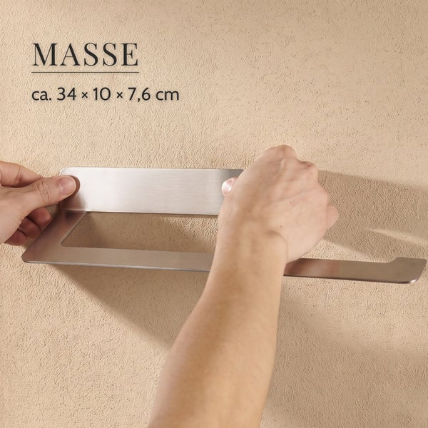 Hände halten einen metallenen Handtuchhalter mit den Maßen circa 34 mal 10 mal 7,6 Zentimeter an eine strukturierte Wand