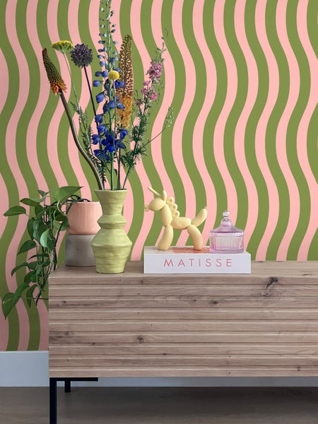 Dekoratives Interieur mit gemusterter Tapete, Kommode, Blumen und dekorativen Objekten.