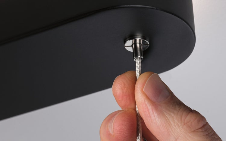 Hand justiert das Stahlseil an einer schwarzen Leuchte.