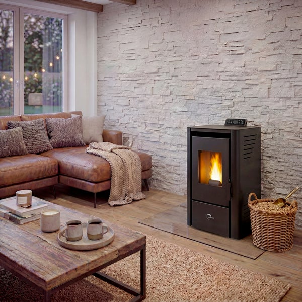 Ein moderner Pelletofen mit sichtbarer Flamme steht in einem gemütlichen Wohnzimmer mit Steinwand, Ledersofa und Holztisch.