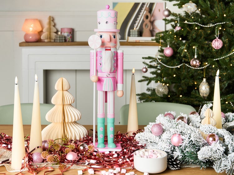 Festliche Dekoration mit einem rosa Nussknacker, Kerzen und einem geschmückten Weihnachtsbaum.