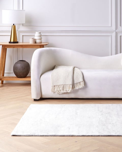 Innenraum mit weißem Sofa, Holztisch, Lampe und Teppich