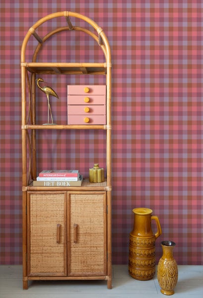 Vliestapete mit Karomuster in Rot und Rosa hinter einem Standregal aus Rattan mit Dekoration und Keramikvasen.