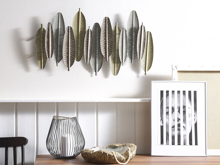 Dekorative Wandkunst mit metallischen Blättern, Windlicht und Dekoschale auf einem Regal.